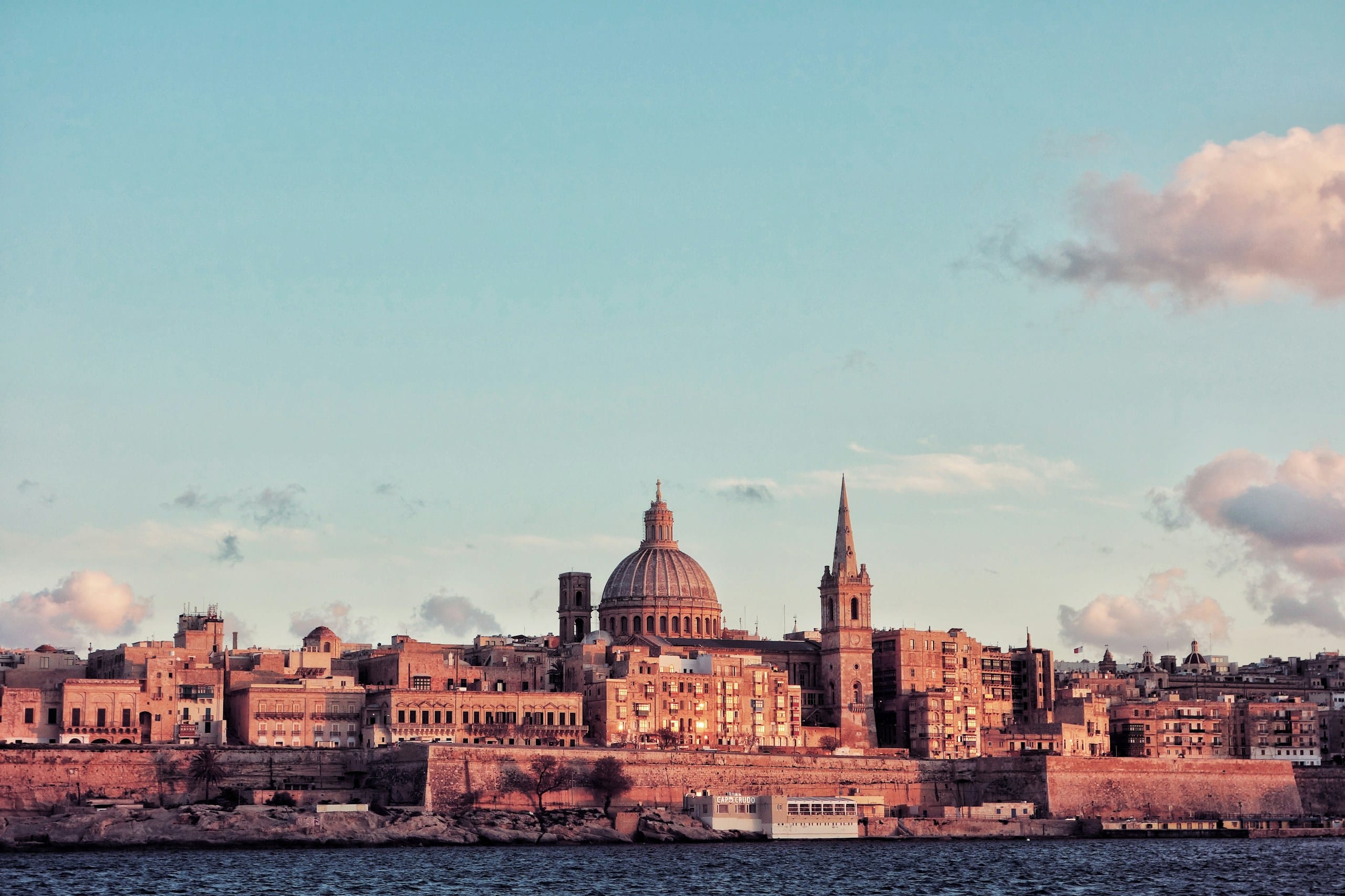 The Valletta skyline at sunset from across Marsamxett Harbour, the dome of the Basilica of Our Lady of Mount Carmel and the spire of St Paul's Anglican Cathedral rising above the bastion walls